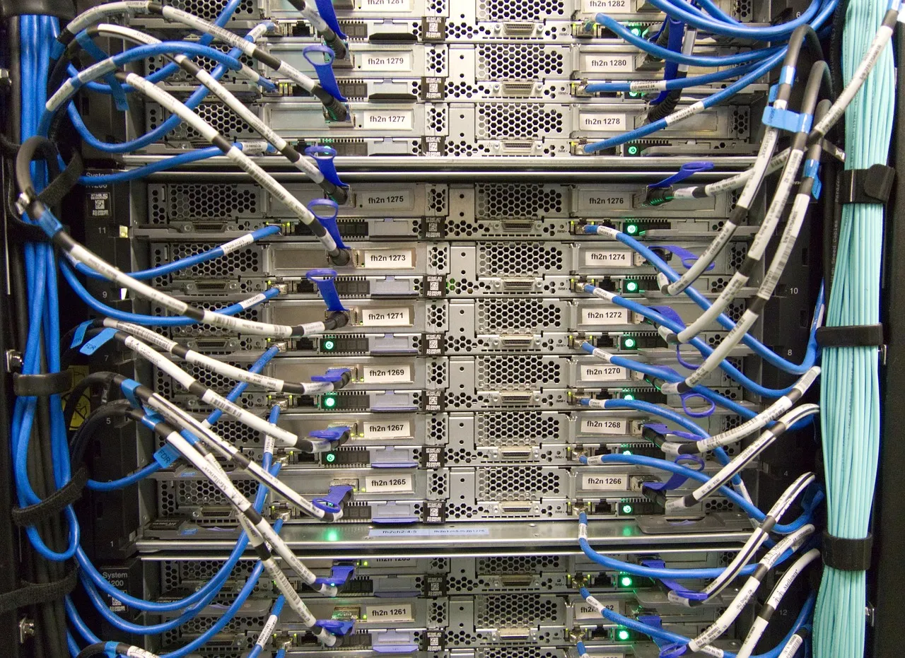 The rear of a server rack, rows of stacked machines with blue and grey network cables running between labelled ports and small green status lights.