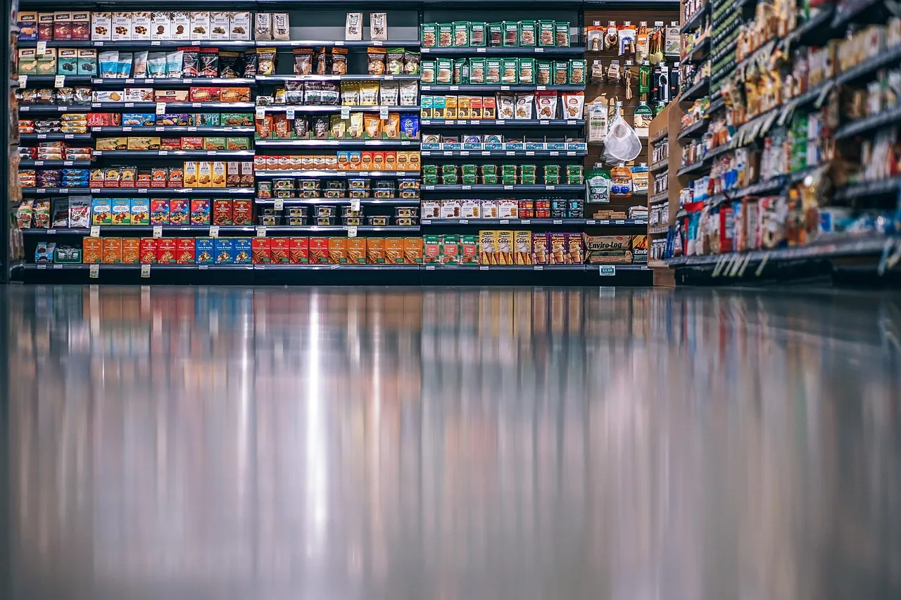 A supermarket aisle of stocked shelves with price labels along each row.