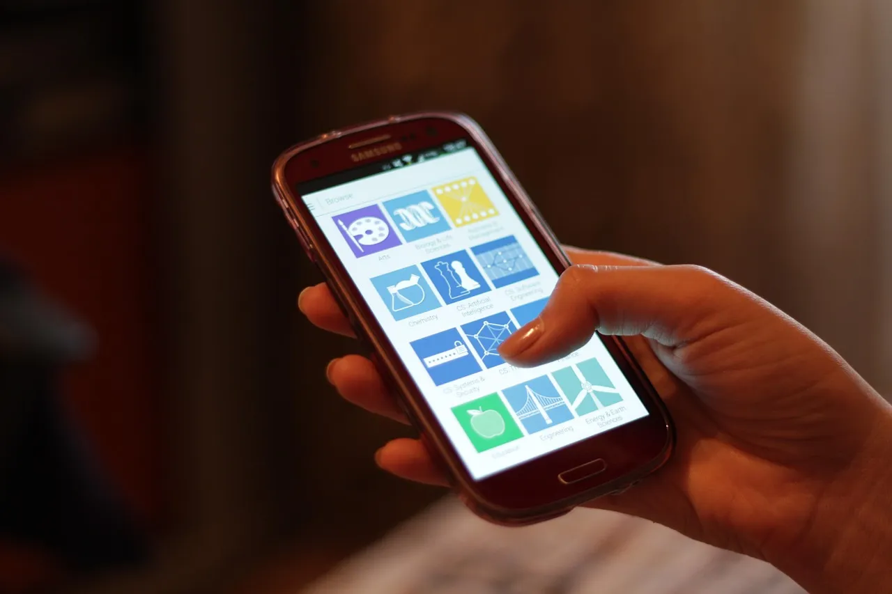 A hand holding a phone showing a grid of app icons — illustrating the store through which a rival marketplace can now be installed.