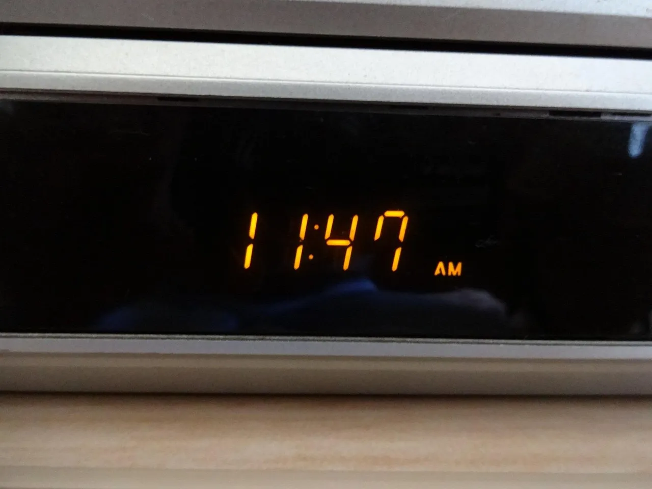 A digital alarm clock display showing 11:47 AM in orange seven-segment digits against a black face