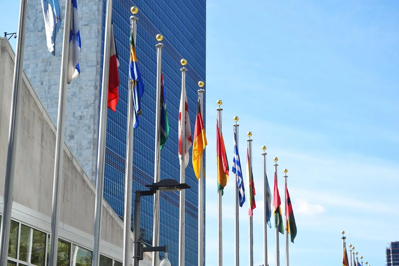 A row of national flags on poles outside a glass-fronted building