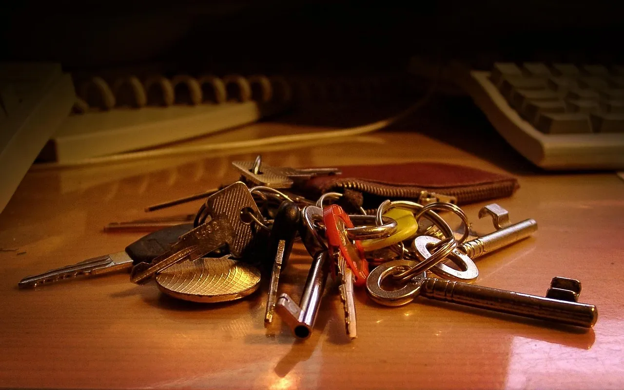 A bunch of keys lying on a desk beside a computer keyboard