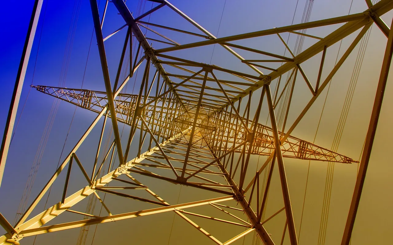 An electricity transmission pylon photographed from directly below against a blue and gold sky, illustrating a report on United States grid interconnection rules.
