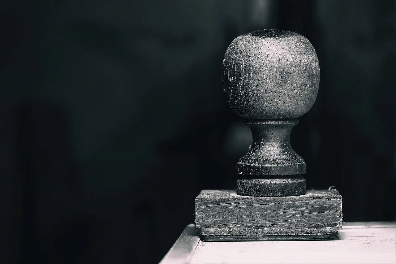 A worn wooden approval stamp resting on a desk, lit low against a dark background.