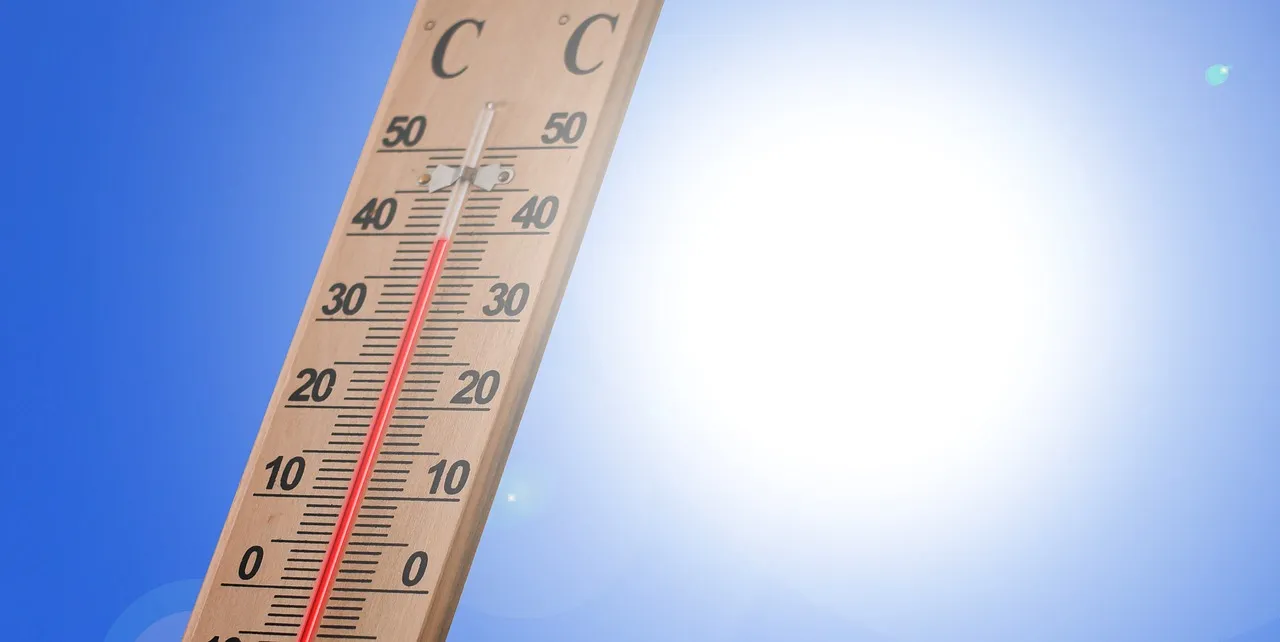 A wooden Celsius thermometer against a blue sky with the sun glaring behind it