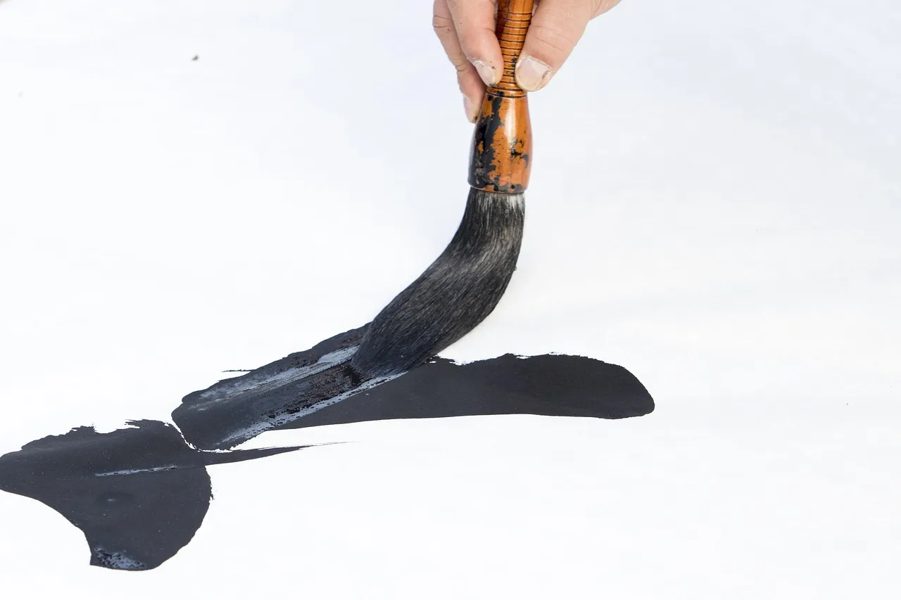 A calligraphy brush drawing a broad black stroke on white paper