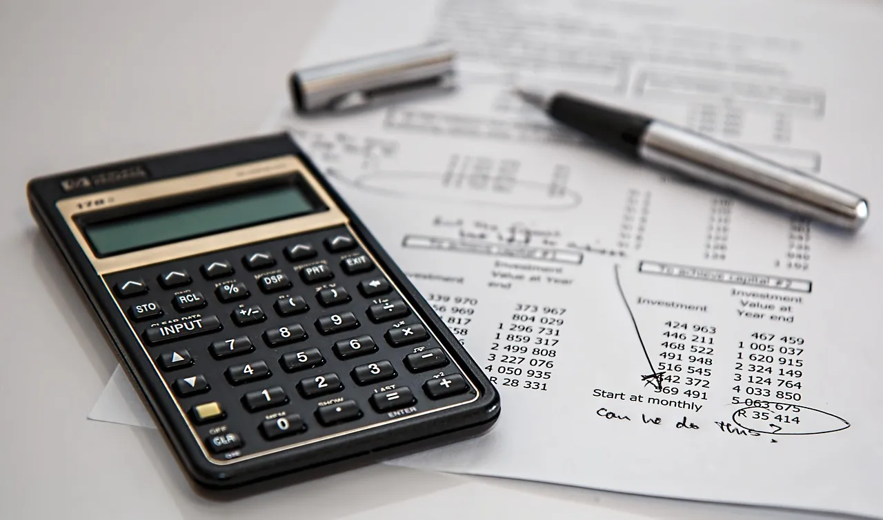 A calculator and a pen lying on printed ledger sheets