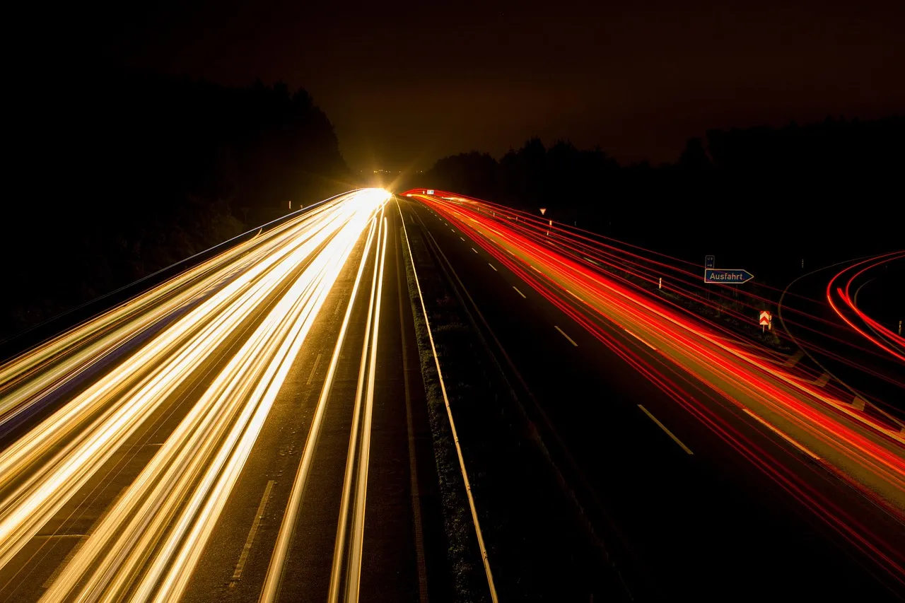 A long-exposure photograph of a motorway at night, headlights and tail lights drawn into continuous streaks — illustrative of traffic measured in volume rather than by who is driving.