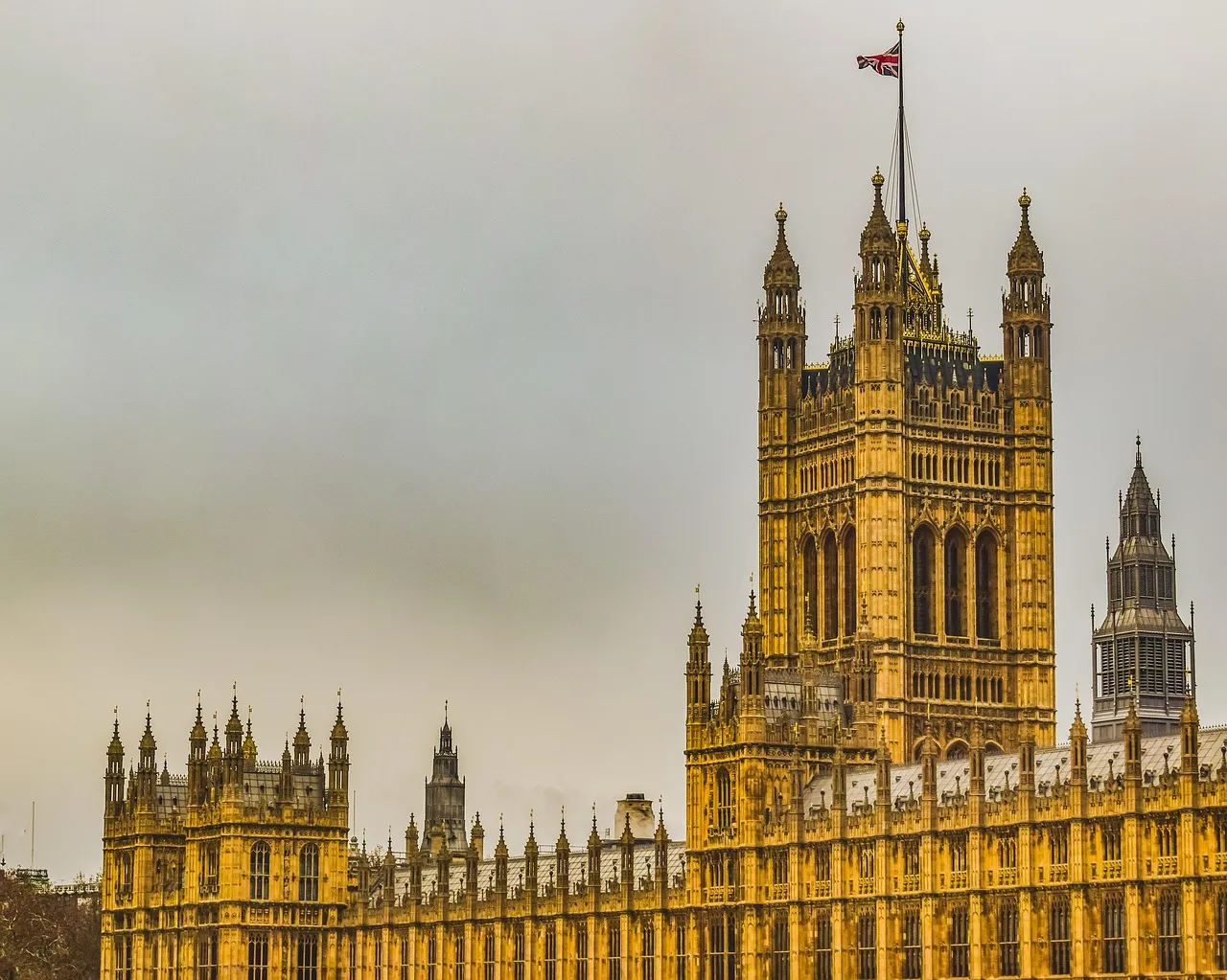 The Palace of Westminster under a grey sky, the Union flag flying from the Victoria Tower