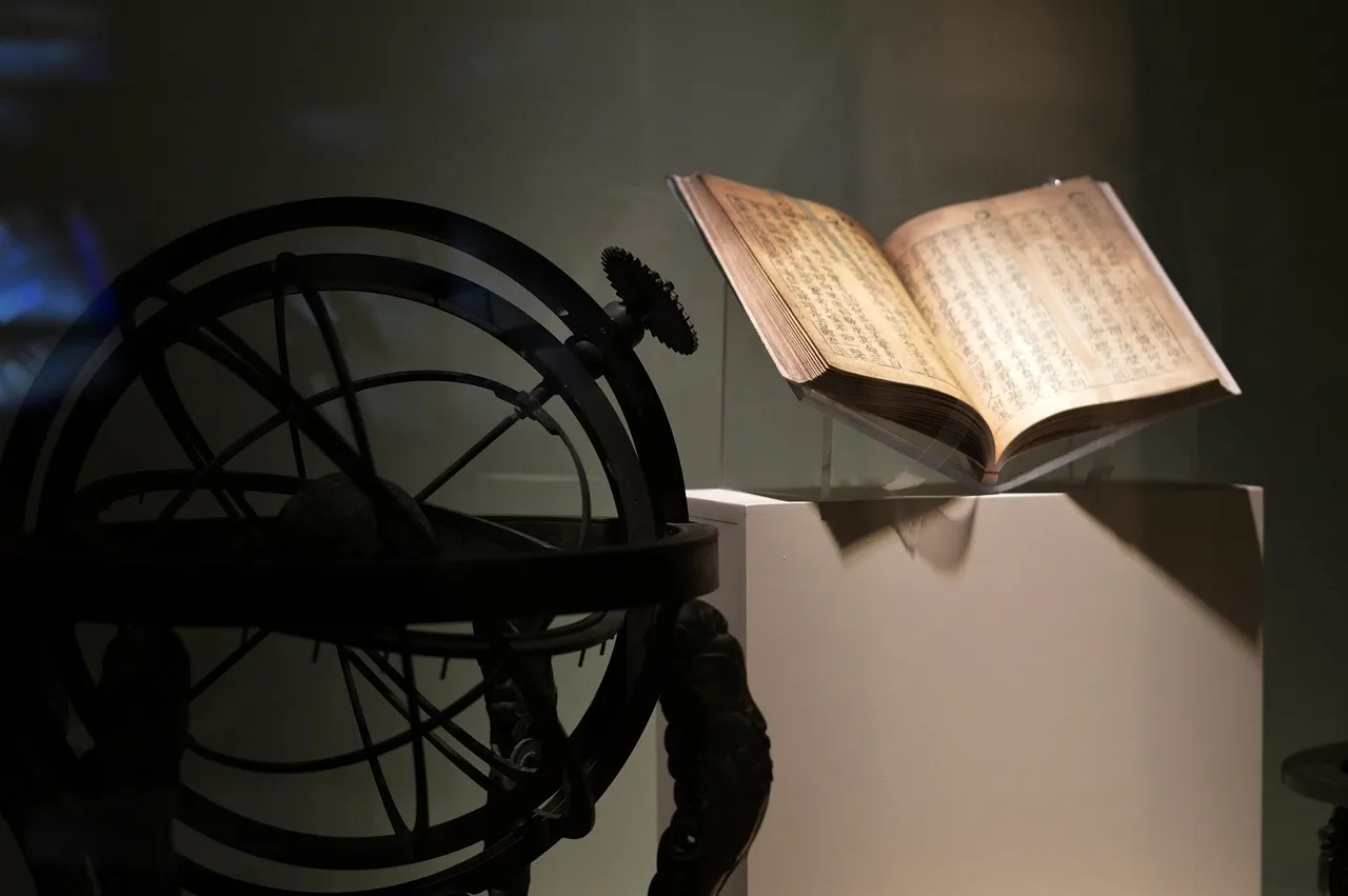 An open antique book beside a metal armillary sphere in low light