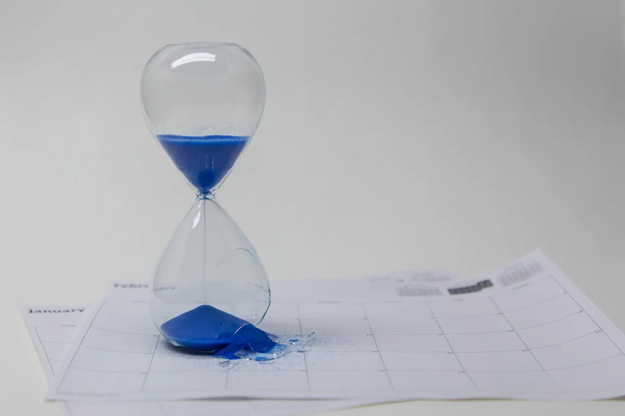 An hourglass of blue sand standing on a calendar page, some sand spilled beside it
