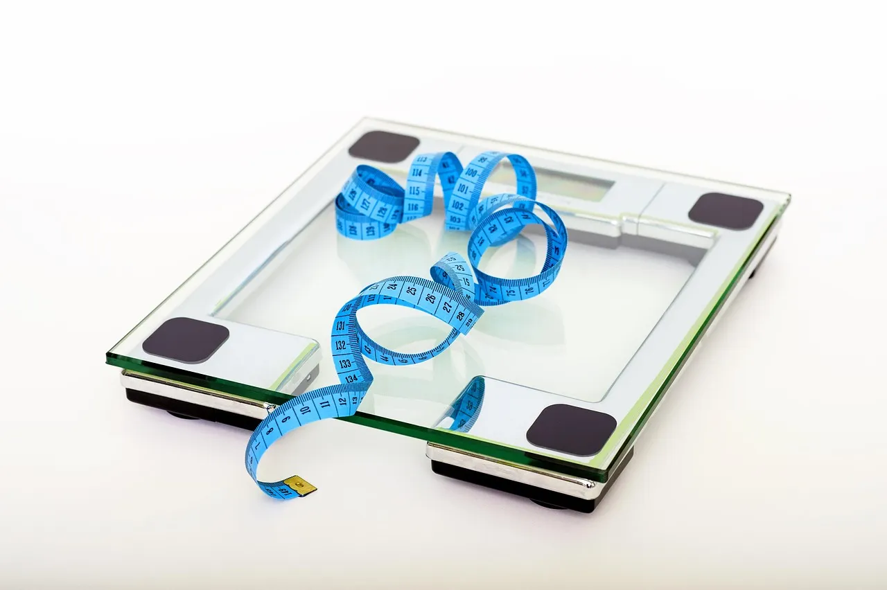 A glass bathroom scale with a blue tape measure on it