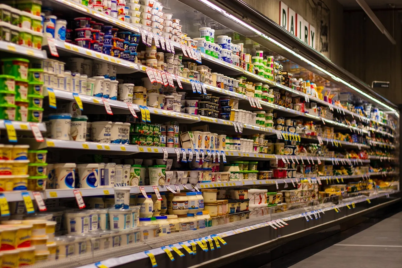 A supermarket chilled dairy aisle, shelves stacked with tubs and cartons under a DAIRY sign