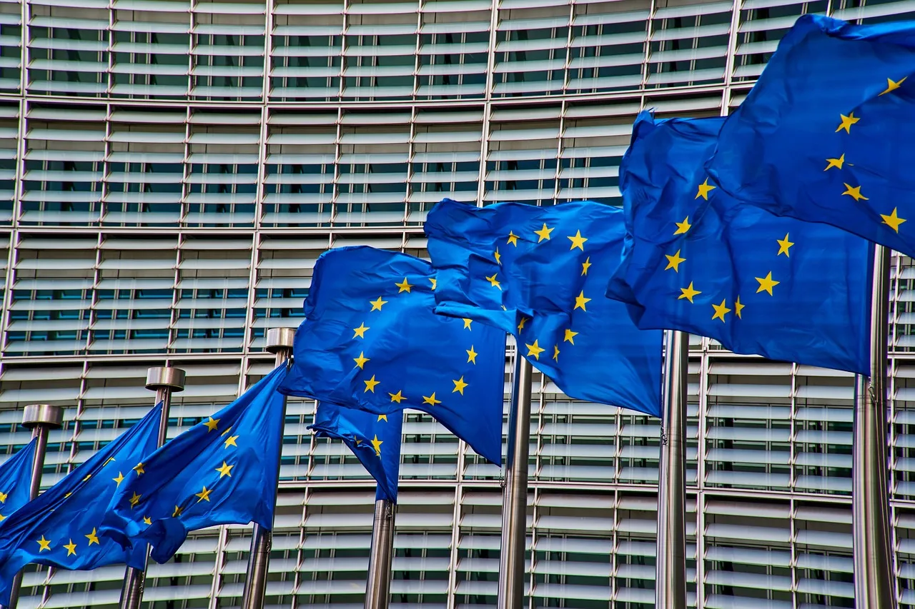 A row of European Union flags flying in front of the curved glass and steel facade of the Berlaymont building in Brussels