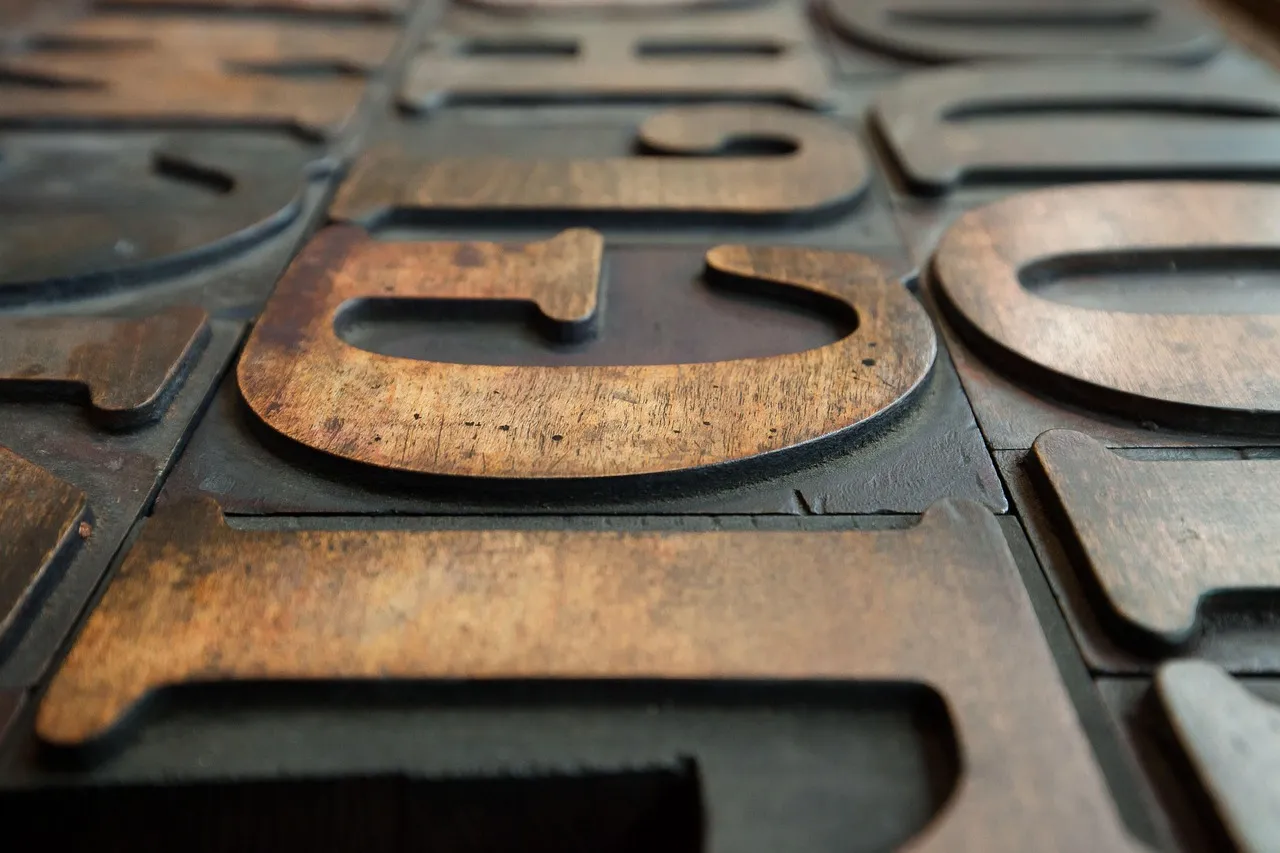 Large wooden letterpress type blocks laid out face up in a tray, each letter a separate physical piece that must exist to be printed