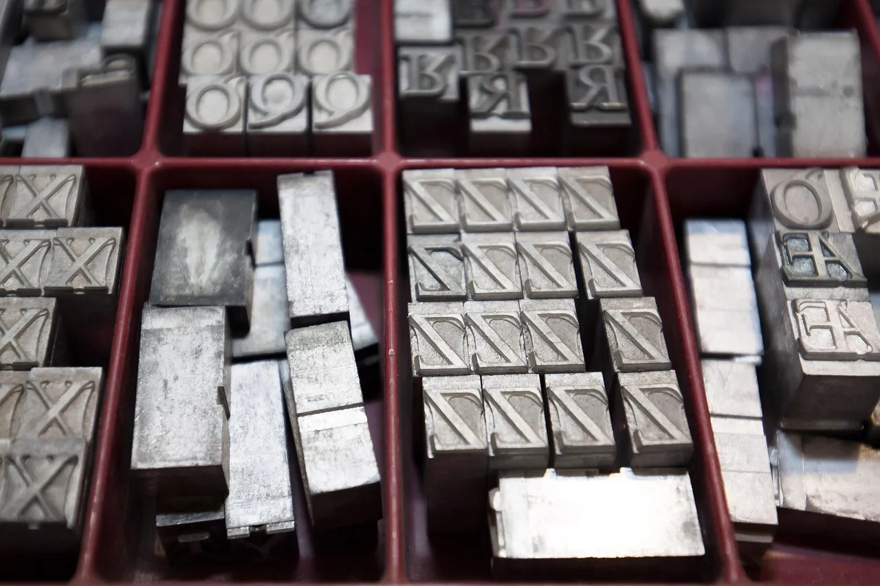 Trays of metal letterpress type seen from above, individual raised letter blocks sorted into red compartments, the nearest ones in sharp focus.