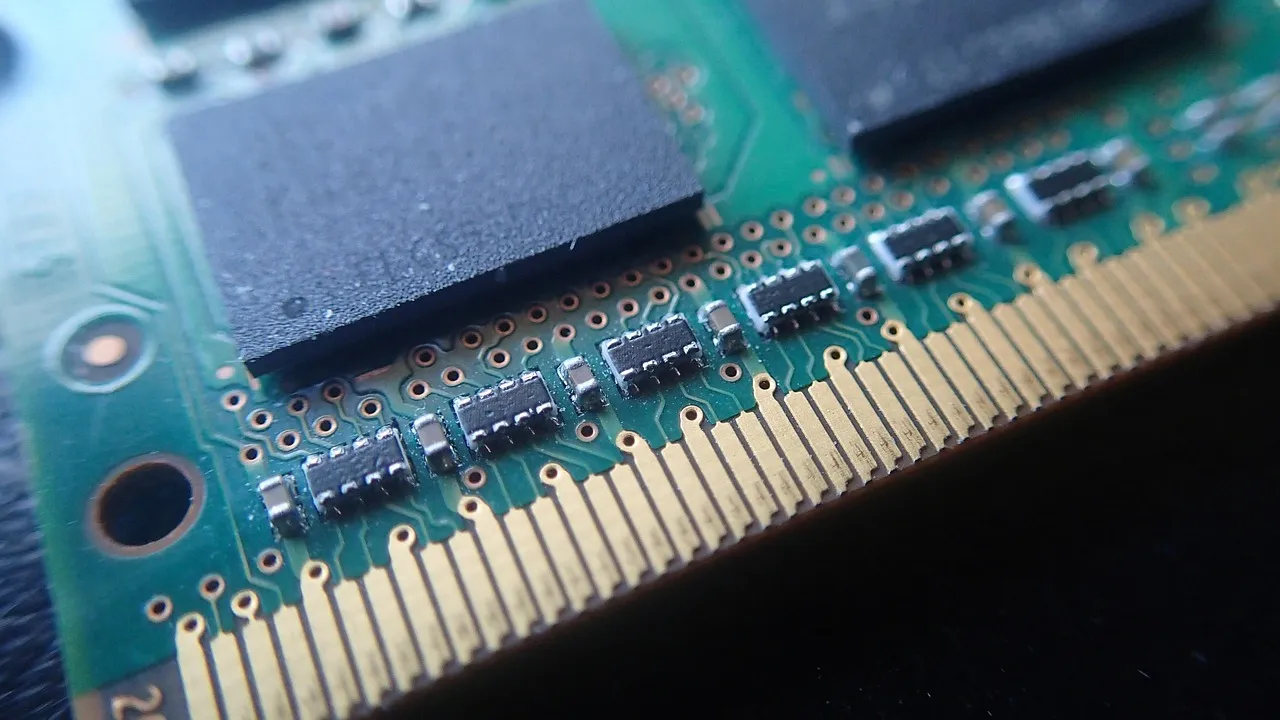 Macro view of a memory module — gold edge contacts along a green circuit board with black DRAM packages above them — the component whose price has risen sixfold in a year.
