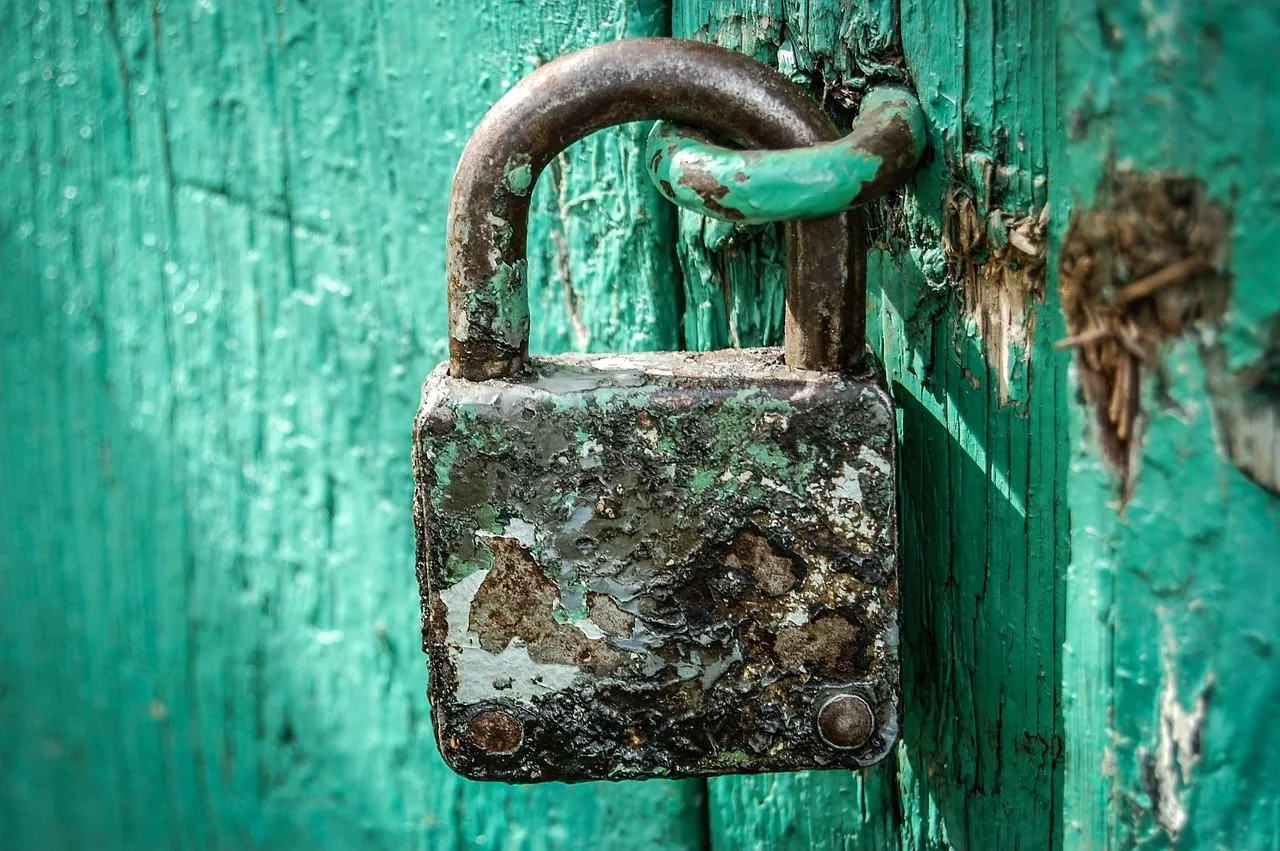 A rusted brass padlock hanging on a weathered green painted door.