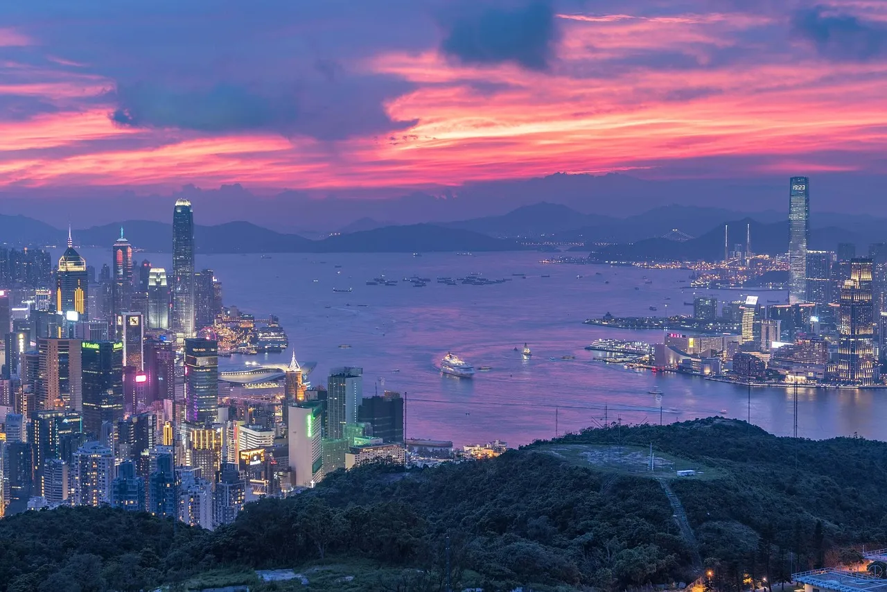 Hong Kong island and Victoria Harbour at dusk under a pink sky, the financial district lit up in the foreground