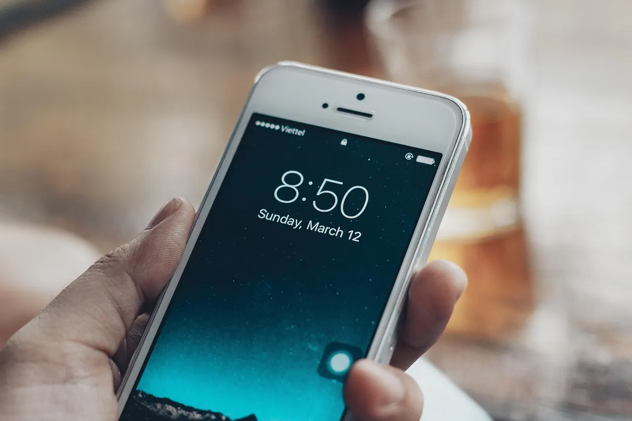 A hand holding an iPhone showing its lock screen