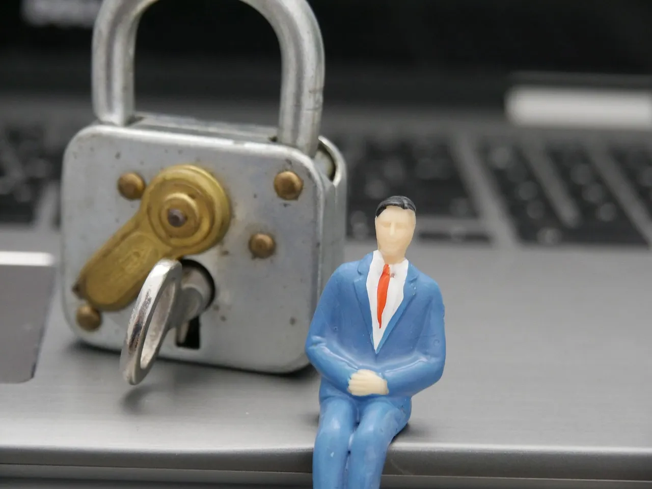 A padlock and a small figurine resting on a laptop keyboard