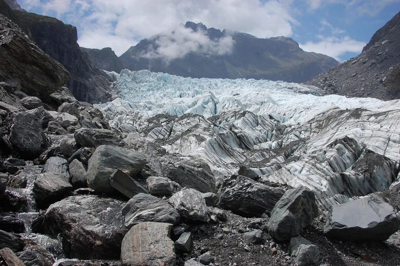 A glacier flowing down a valley above a field of grey boulders