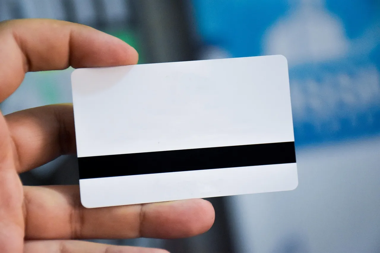 A hand holding a blank white plastic card with a magnetic stripe, bearing no name or number
