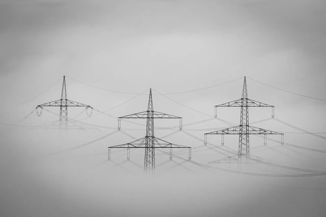 Three high-voltage transmission pylons standing in thick fog, their power lines fading into white, photographed in monochrome