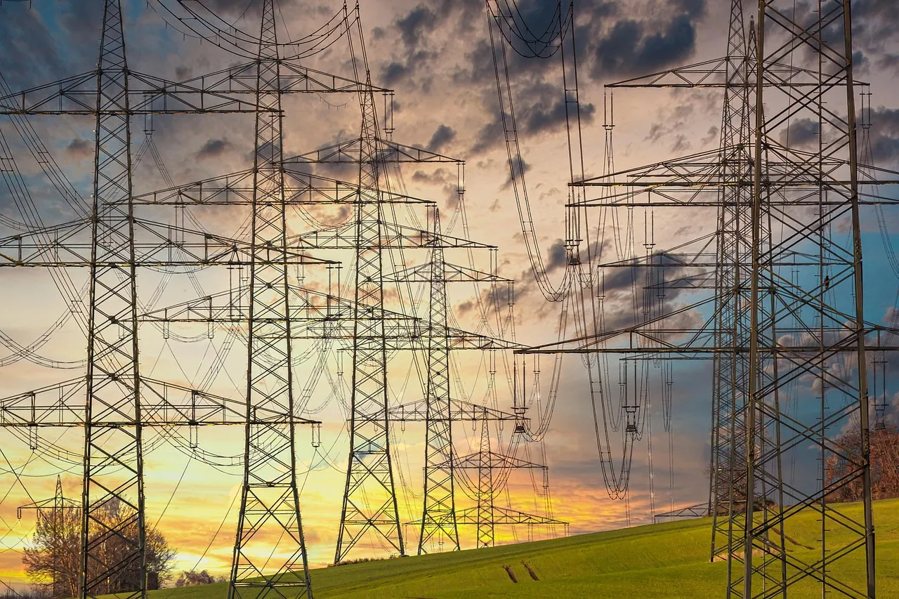 Rows of transmission pylons carrying power lines across a field at sunset