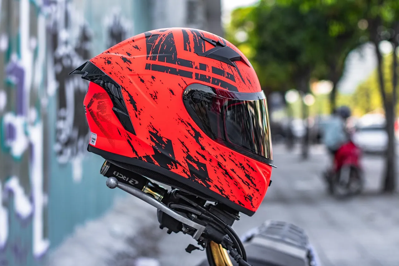 A red and black full-face motorcycle helmet resting on a parked bike in a street