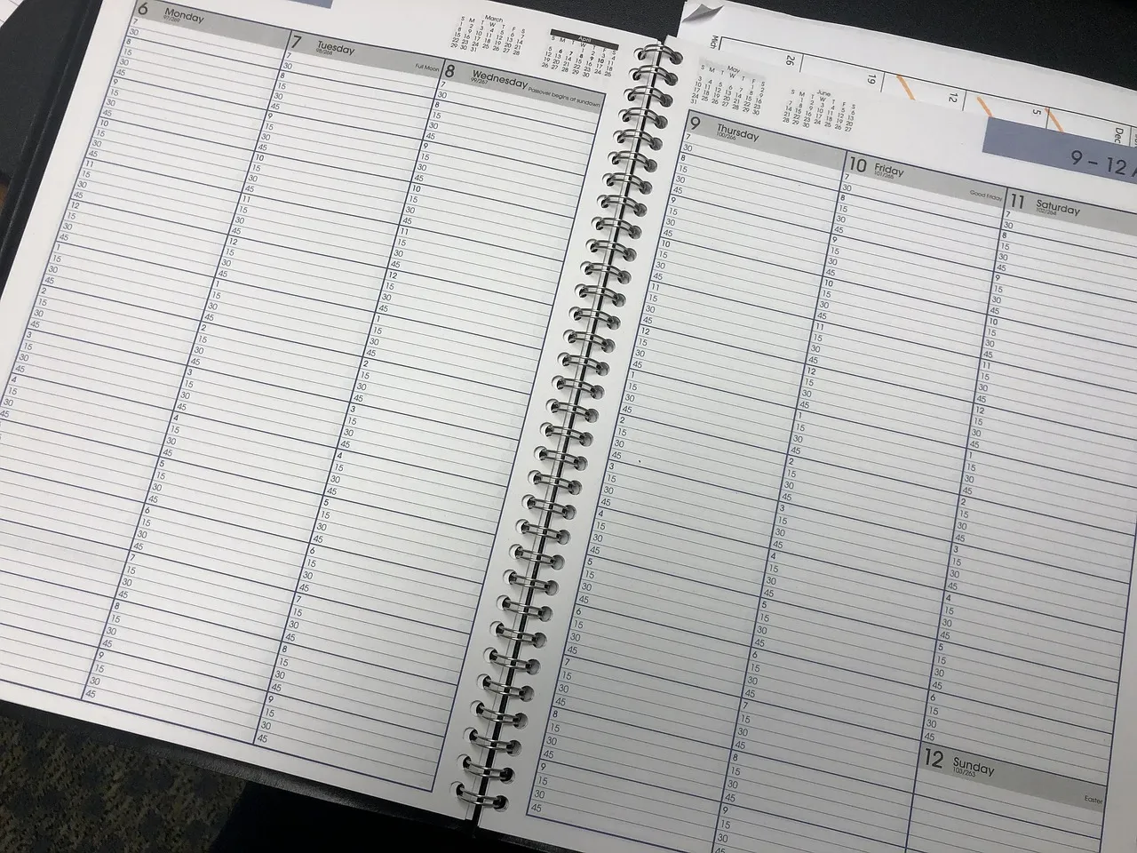 An open spiral-bound week-to-view planner lying flat on a desk, every ruled line for every day left blank