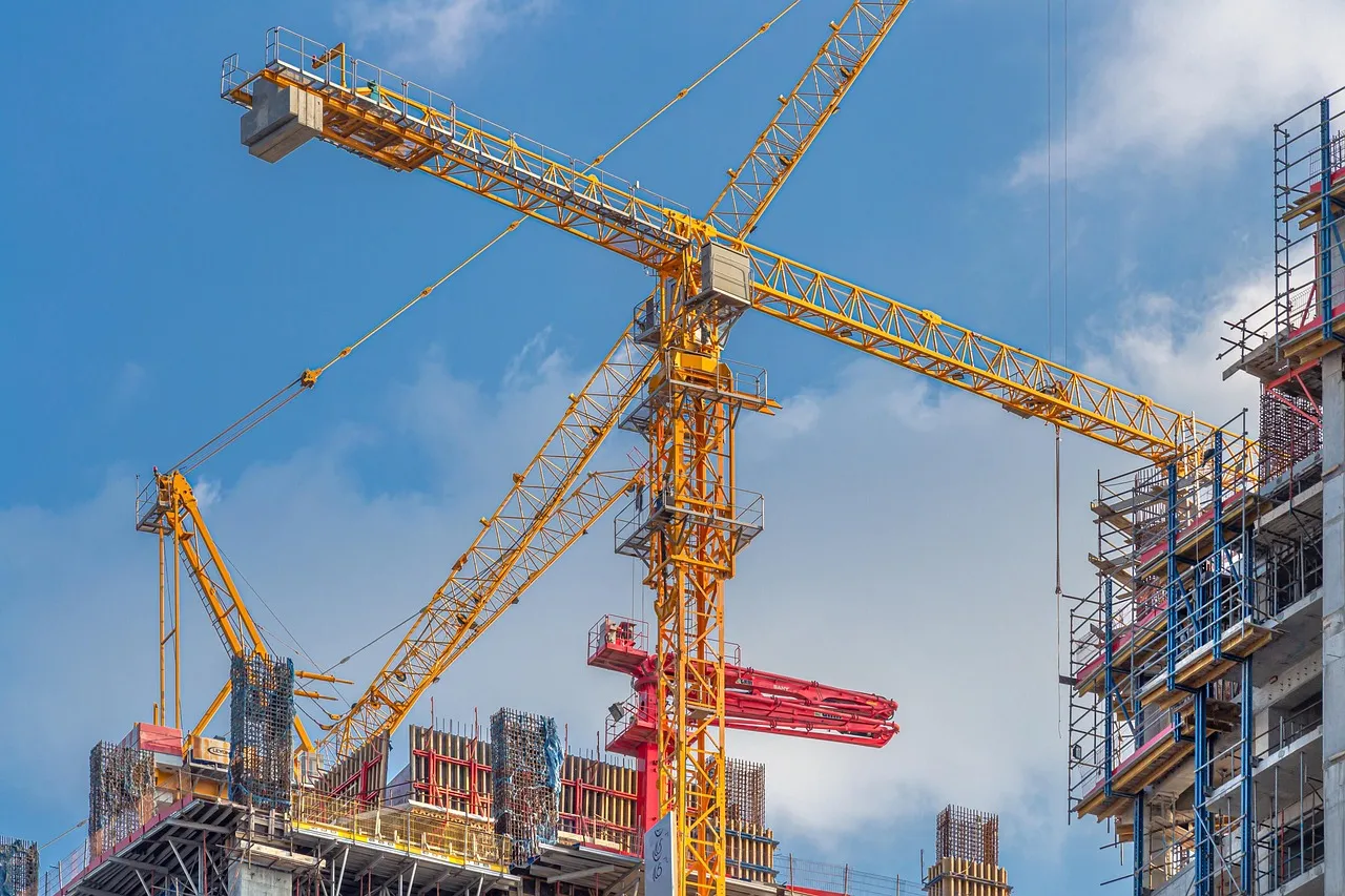 Two tower cranes above an unfinished concrete building against a blue sky