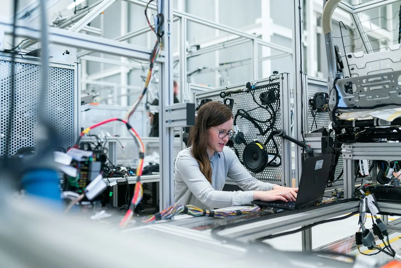 An engineer working at a laptop beside electronics test rigs, illustrating a report on component costs in Xiaomi's handset margins.