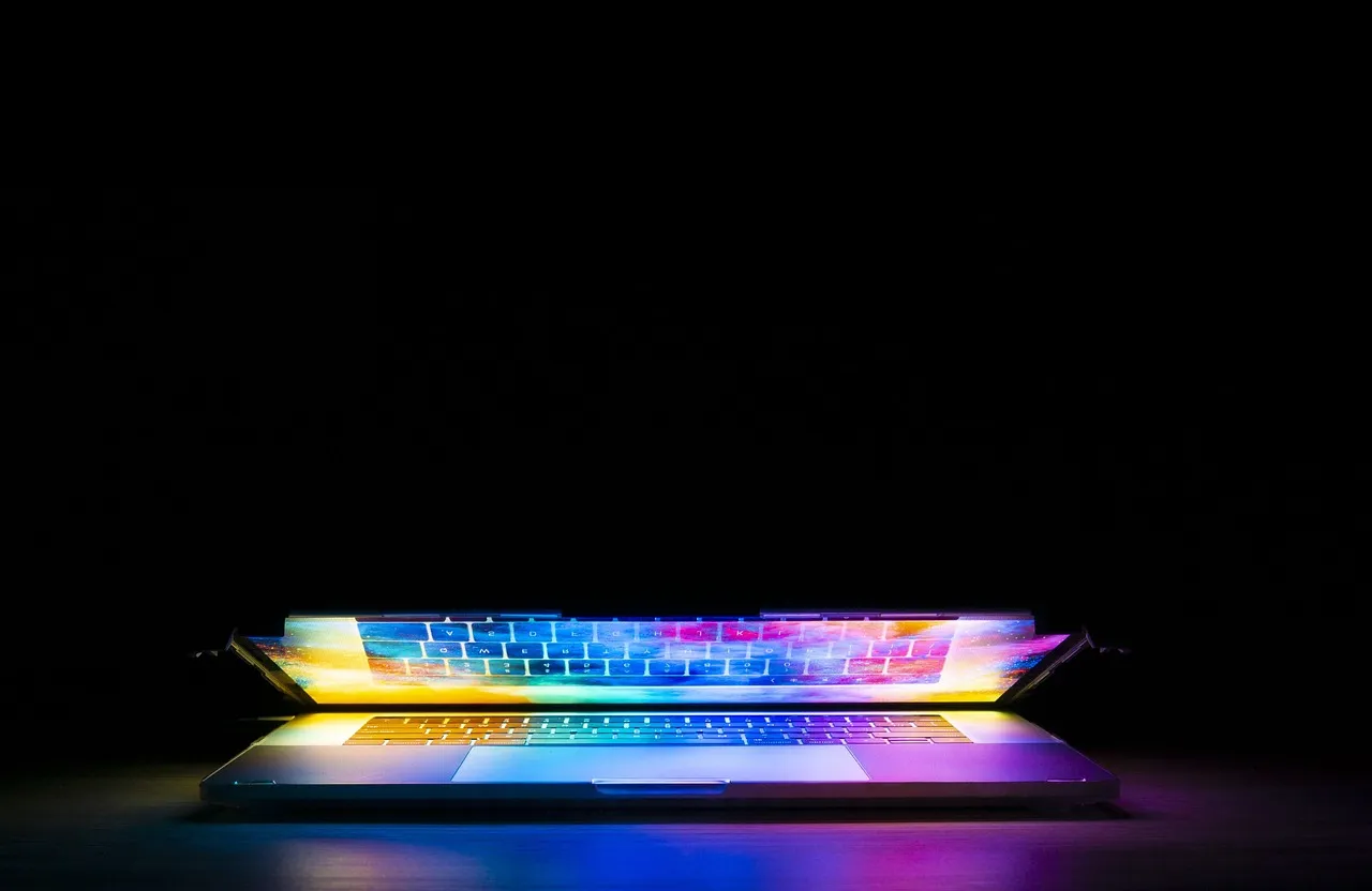 A partly closed laptop with its backlit keyboard glowing in a dark room