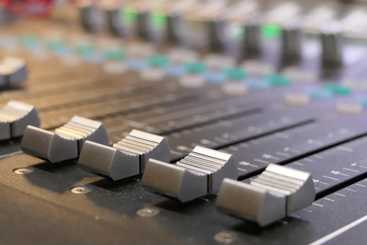 Illustrative: a close-up of channel faders on a studio mixing console, with indicator lights behind them.