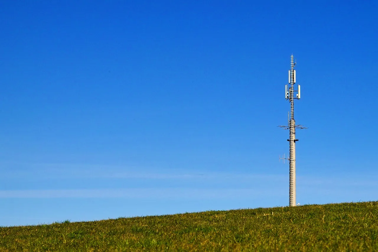 A single mobile telephone mast standing on a grassy hill against a clear blue sky