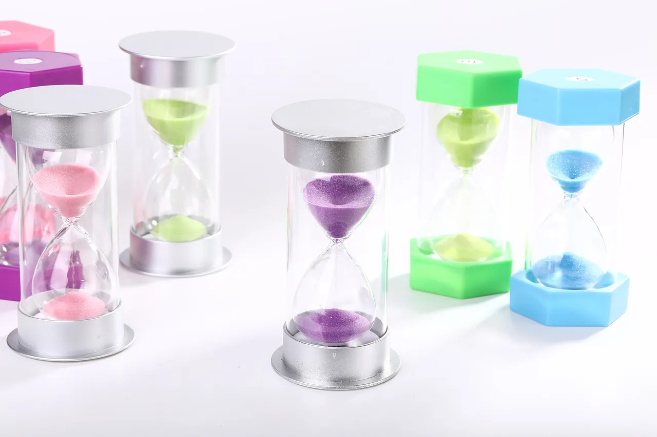 Several small sand timers in different colours arranged on a plain white surface
