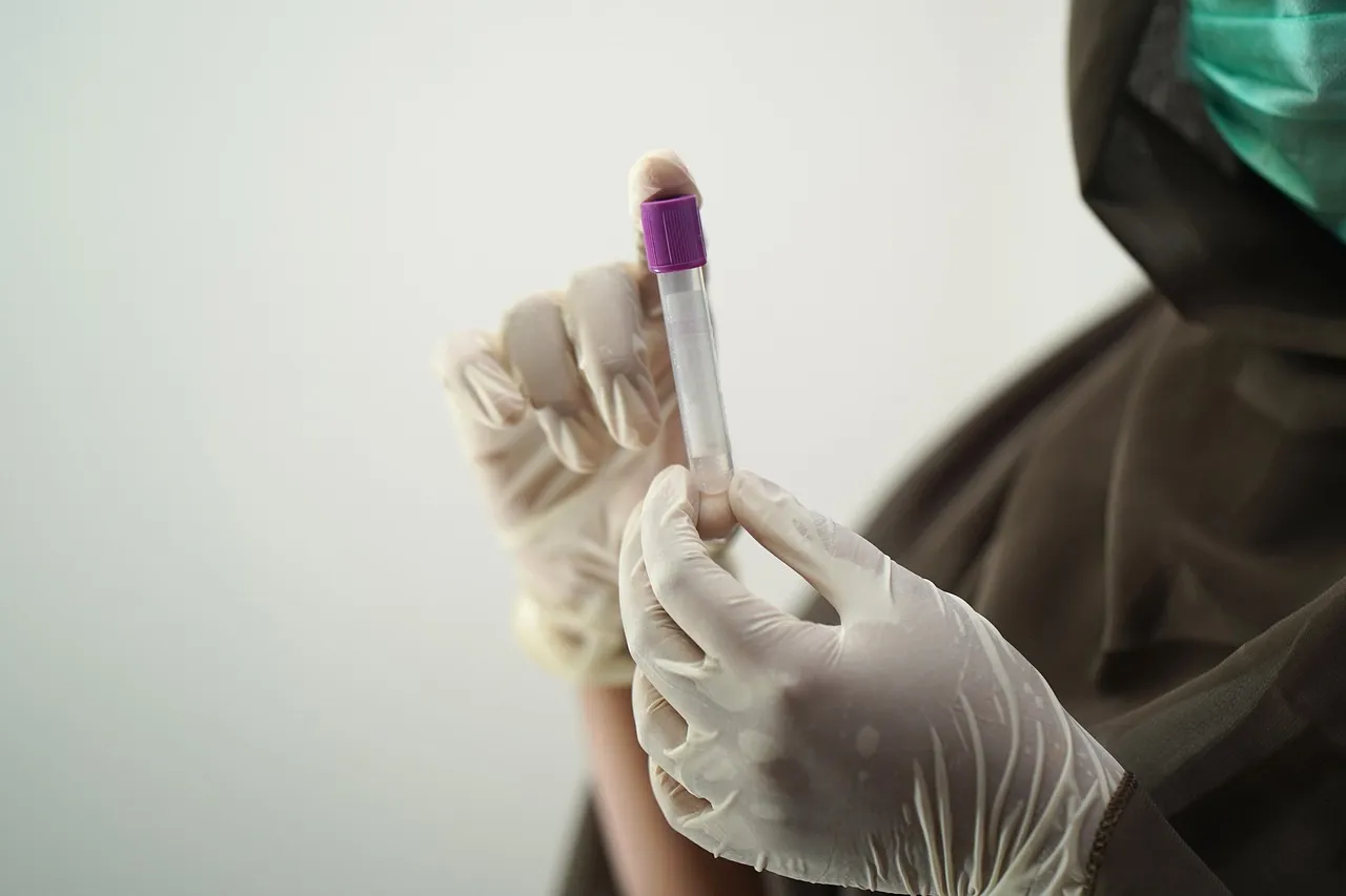 A gloved hand holding a capped blood sample tube in a laboratory.