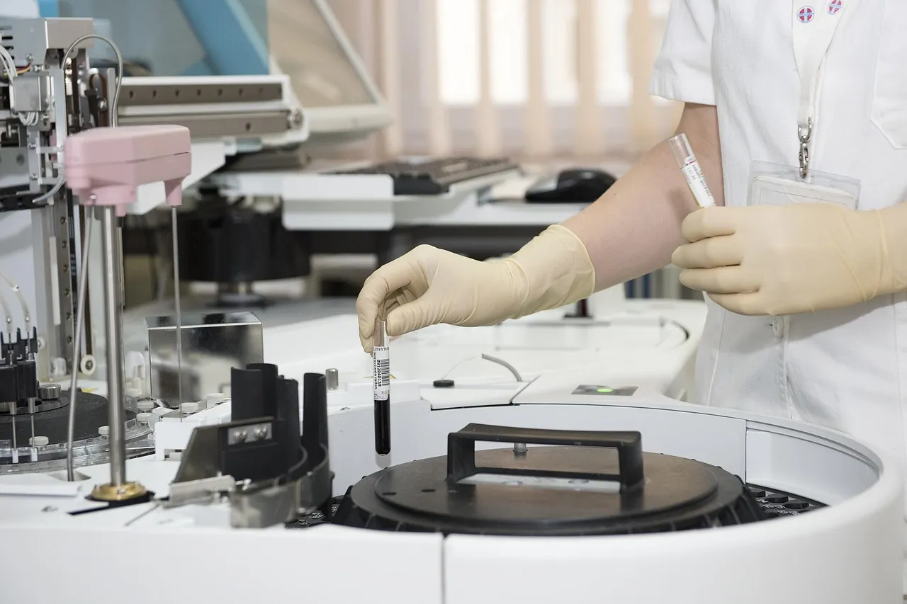 A gloved laboratory worker loading a sample tube into an automated analyser