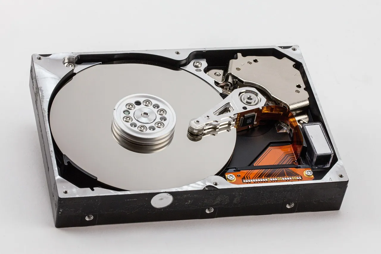 An opened hard disk drive showing its platter and read arm, on a white surface