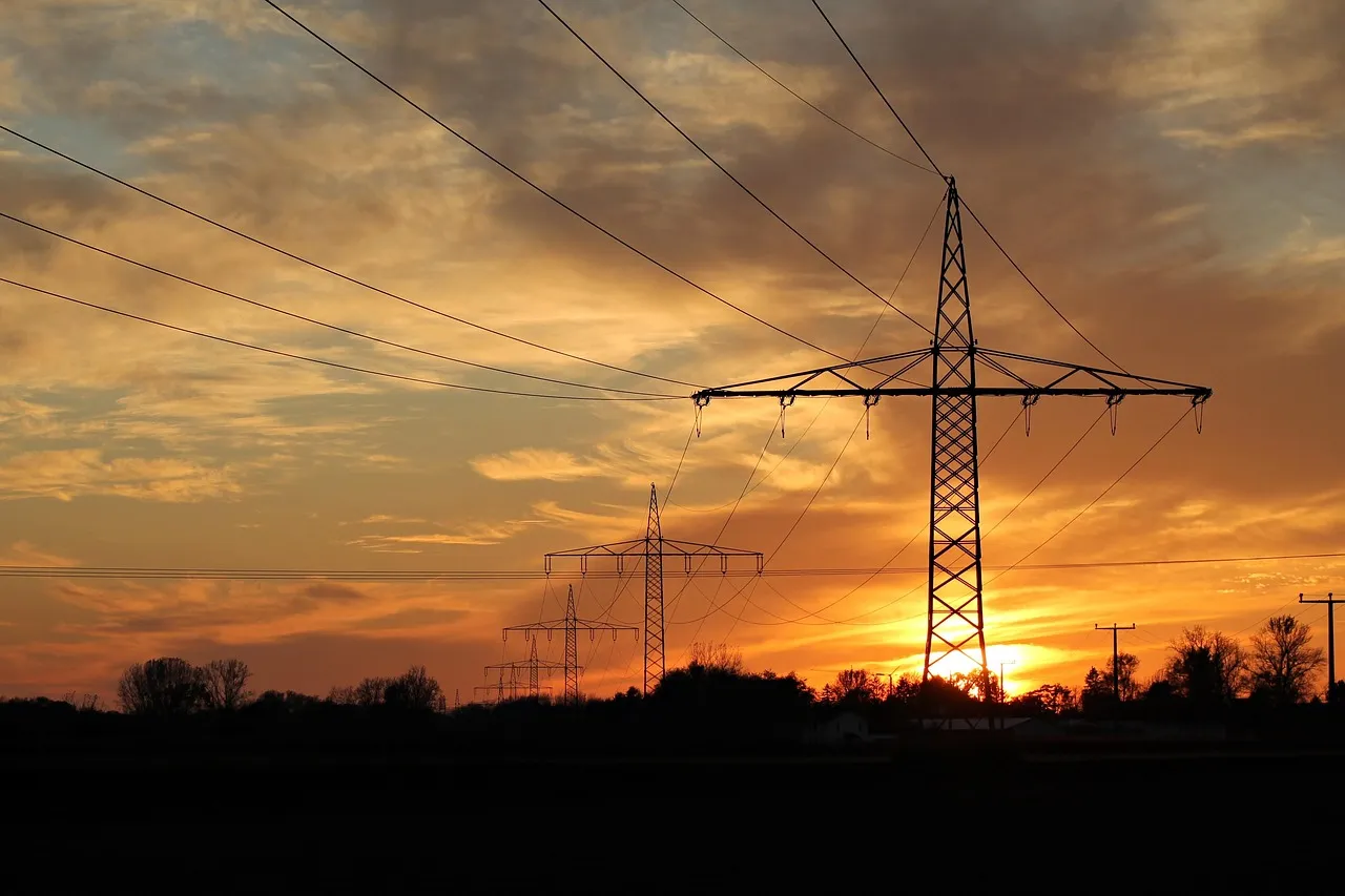 Electricity transmission pylons and power lines silhouetted against an orange sunset
