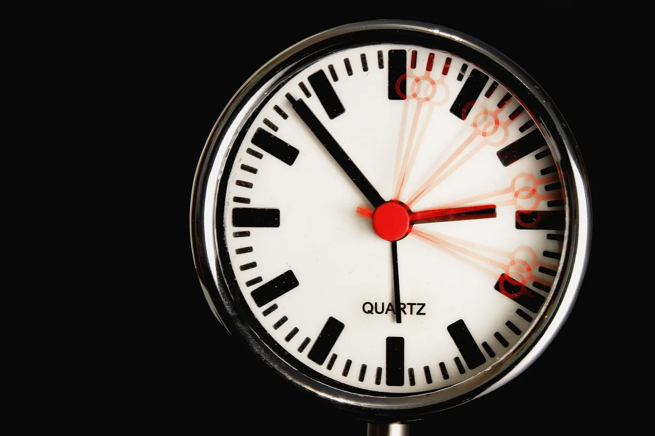 A close-up of a clock face against a black background, the red second hand blurred across several positions