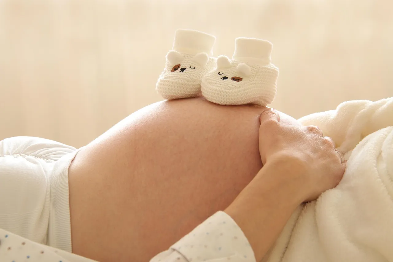 A pair of white knitted baby booties resting on a pregnant woman's belly
