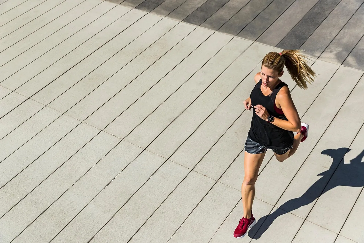 A runner seen from above, mid-stride on a pale boardwalk, a long shadow alongside