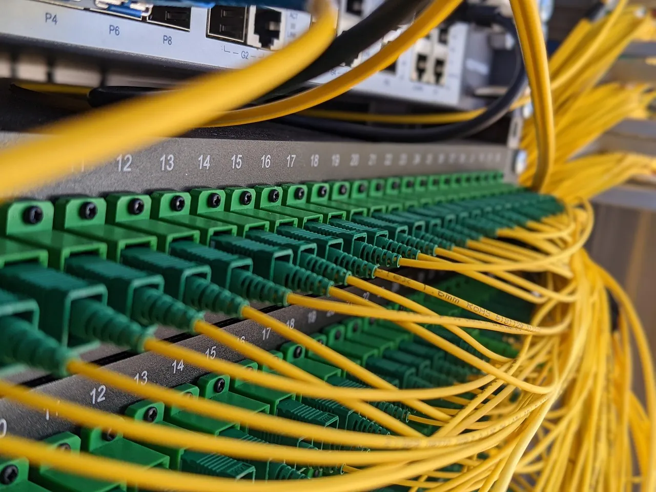 Rows of numbered ports on a fibre patch panel, green connectors threaded with yellow leads — illustrative of the networked estate a three-day patch deadline has to cover.
