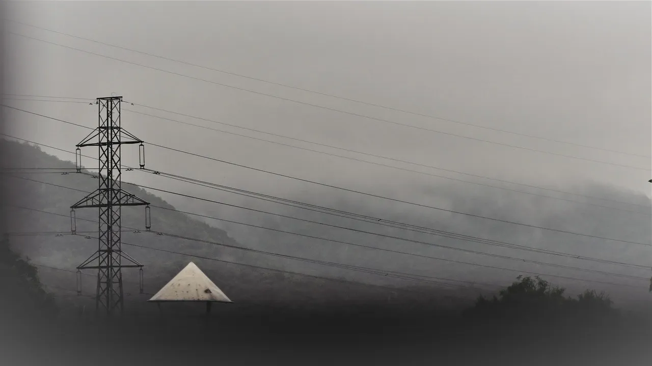 A steel electricity transmission pylon carrying high-voltage lines across a misty hillside