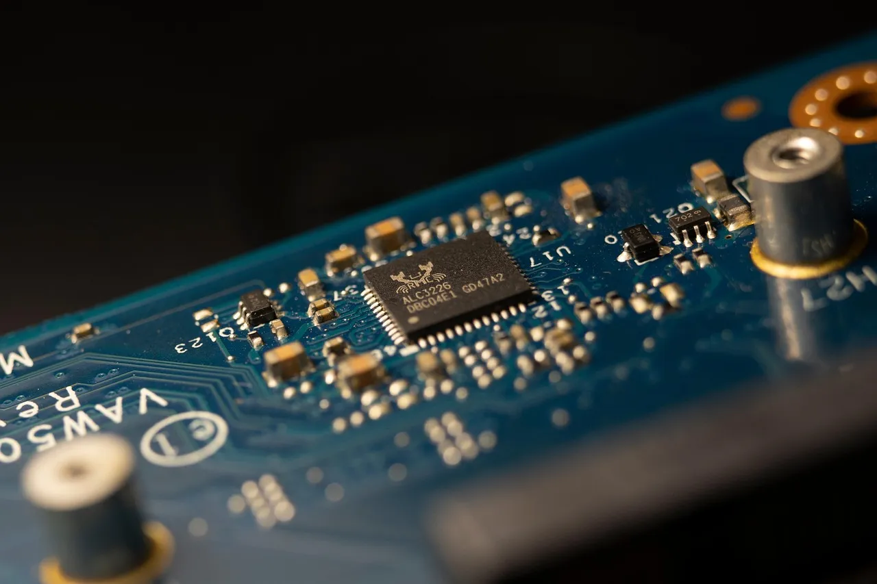 Close-up of a single packaged integrated circuit soldered to a blue circuit board, pins fanning out to gold pads — illustrative of the model-specific silicon at the centre of the deal.
