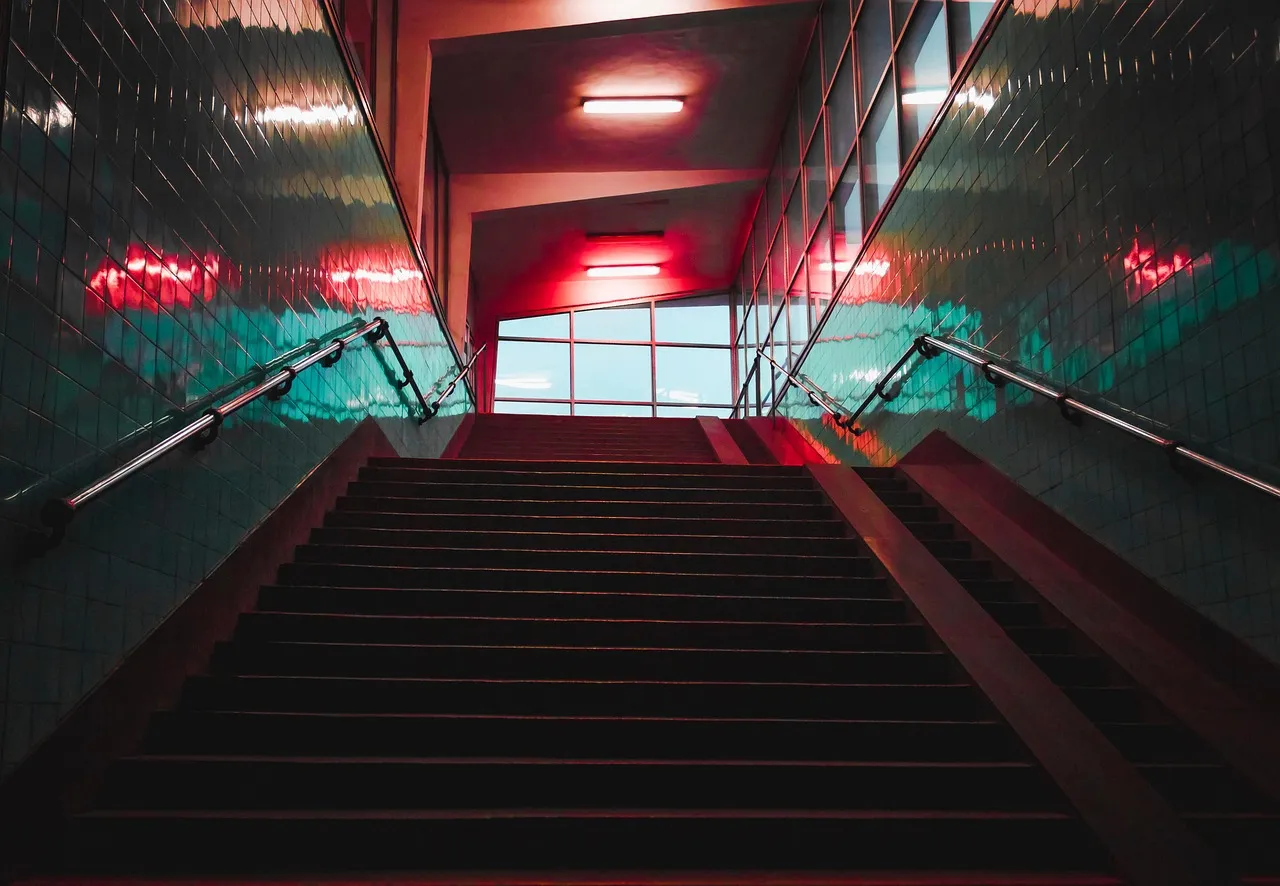A long flight of stairs photographed from the bottom, rising through tiled walls towards daylight at the top