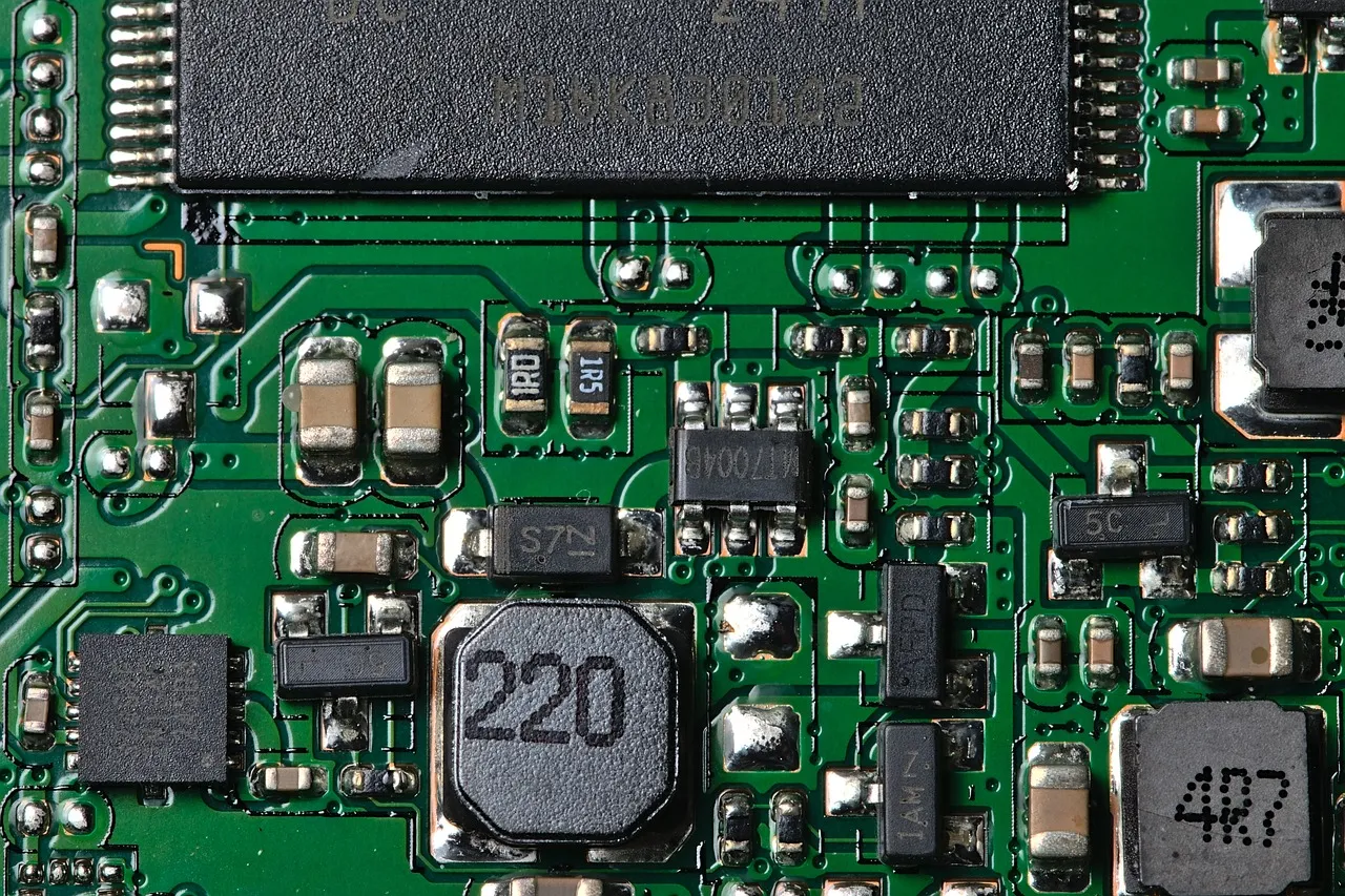 Close view of a green printed circuit board showing a large black memory package, shielded inductors marked 220 and 4R7, and rows of surface-mounted components
