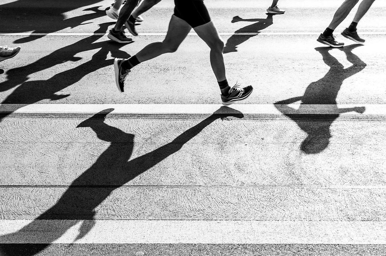 Runners' legs and long shadows on a sunlit road, in black and white